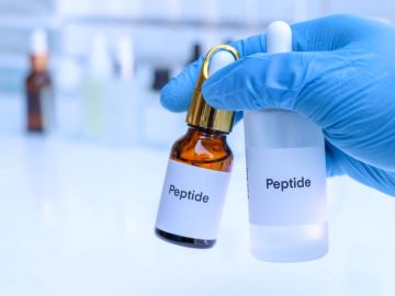 Gloved hand holding two peptide bottles in a lab setting.