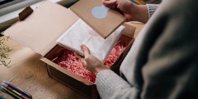 Person unpacking a gift box with a card and shredded paper.