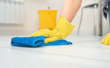 Hand in yellow gloves cleaning floor with blue cloth.