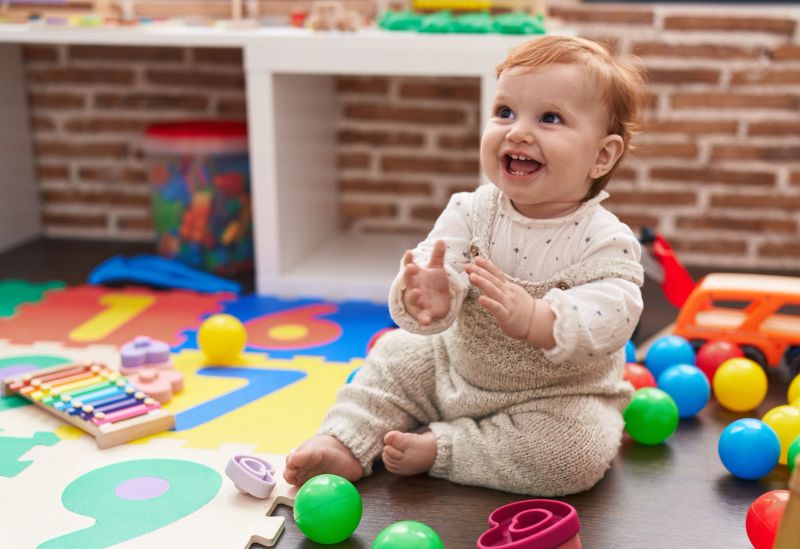 Adorable redhead toddler sitting on floor applauding at kindergarten