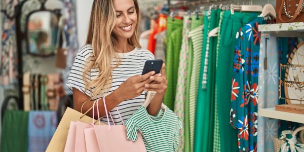 Smiling woman holding shopping bags and phone in clothing store.