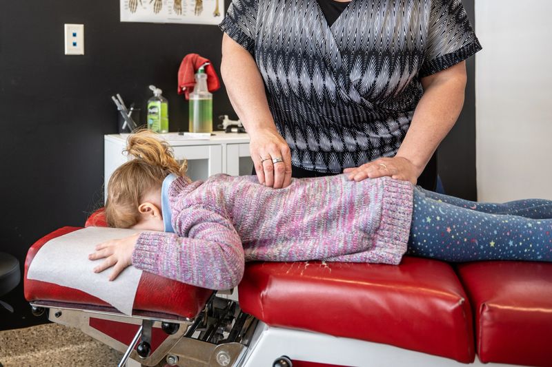 A preschool girl is getting a chiropractic adjustment on a table in a doctors office
