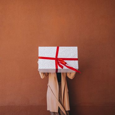 Person holding a large gift box in front of their face against a brown wall.
