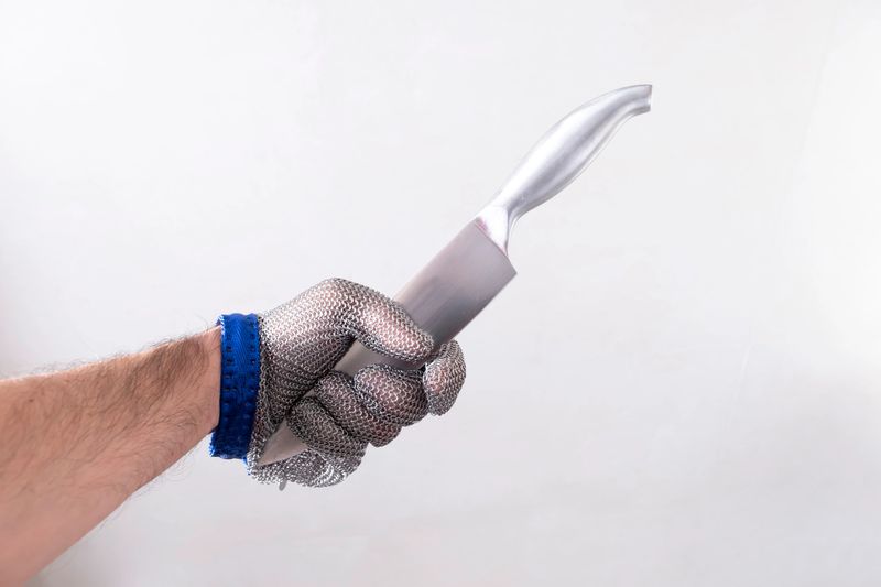 one hand with protective glove, glove of butcher of wire metallic mesh, holding a kitchen knife by the sharp edge, anti cut protection, horizontal