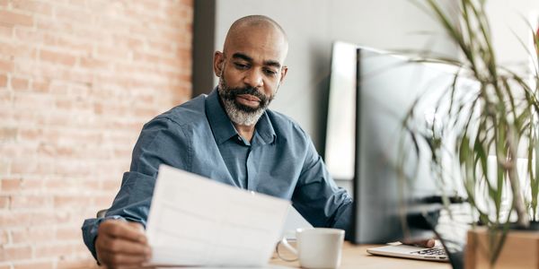 Man reviewing documents at his desk with computer and coffee cup.