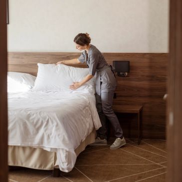 Person making a bed in a hotel room.