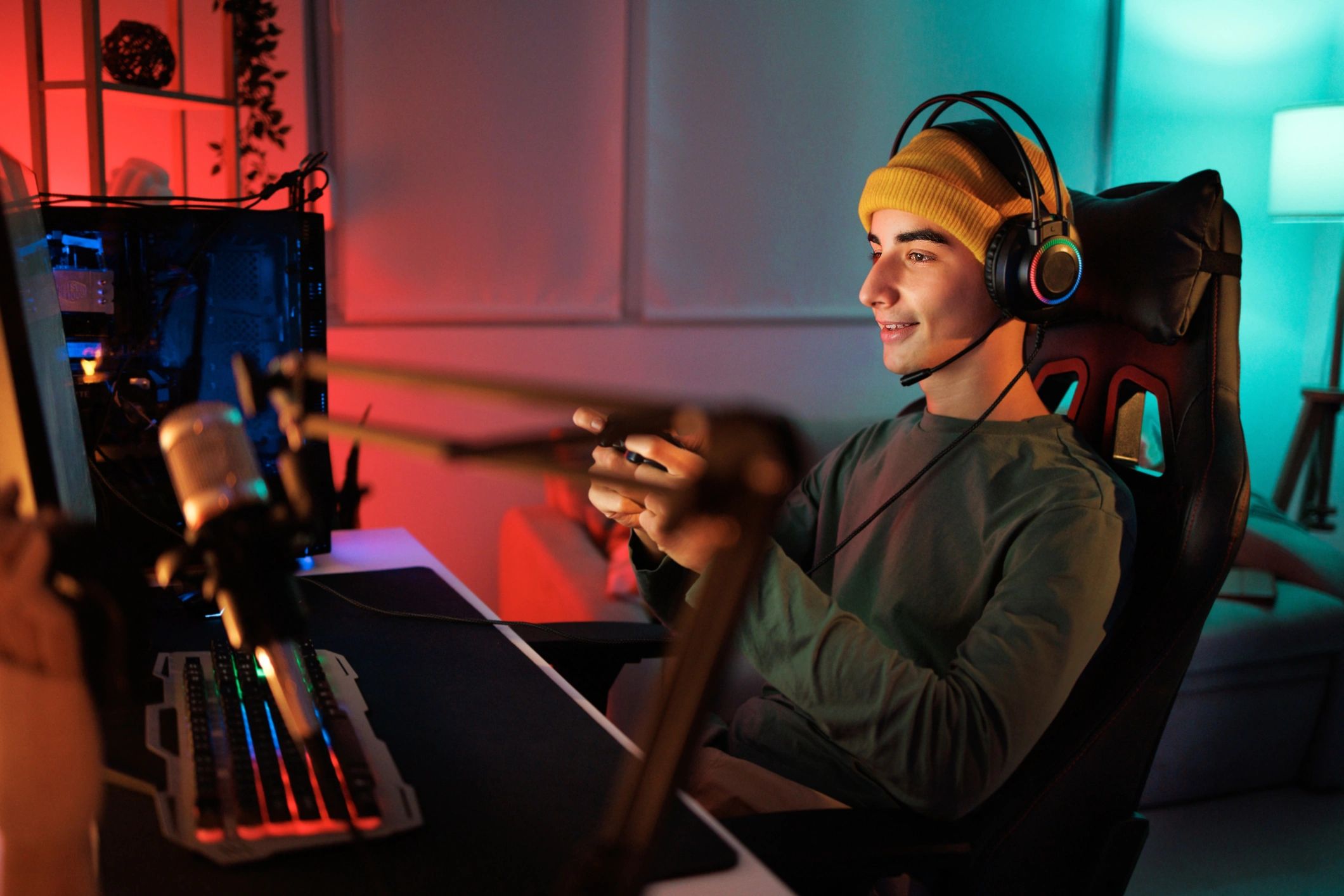Young gamer wearing a yellow beanie and headset playing video games.