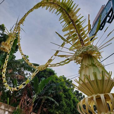 Tall traditional Balinese penjor decoration against a blue sky.