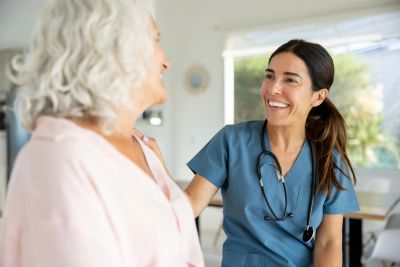 Nurse smiling at elderly woman in a home setting.