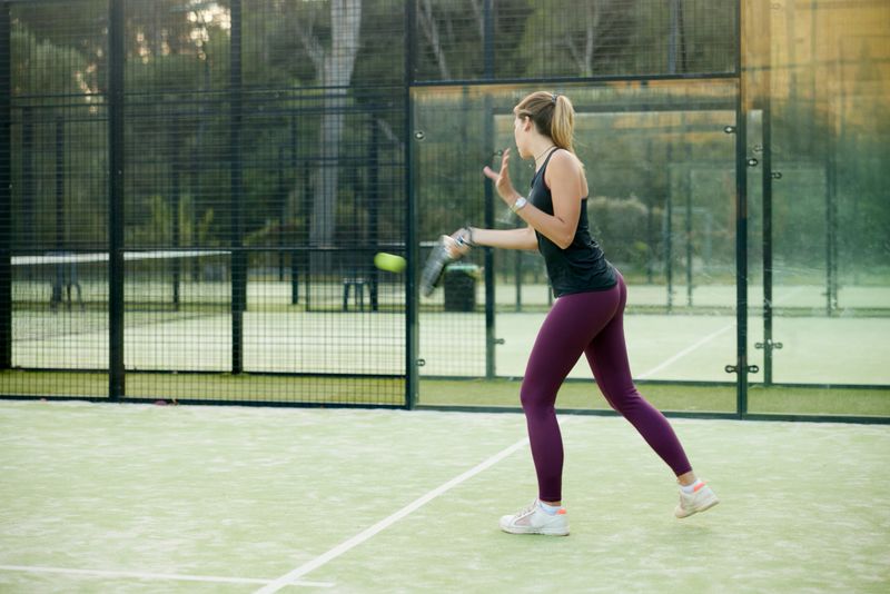 Side view of young fit adult female returning a ball during padel match. Side view, copy space, full length