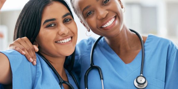 Two smiling healthcare workers in scrubs with stethoscopes.