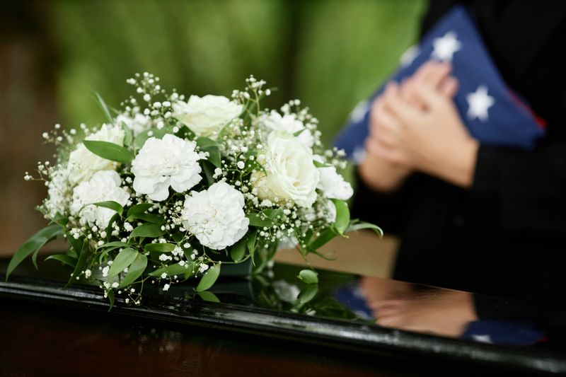 Close up of flowers on coffin at outdoor funeral ceremony for army veteran, copy space