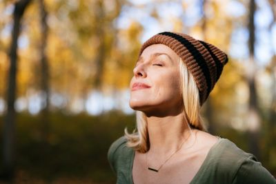 Woman enjoying autumn sun with eyes closed, wearing a striped beanie.