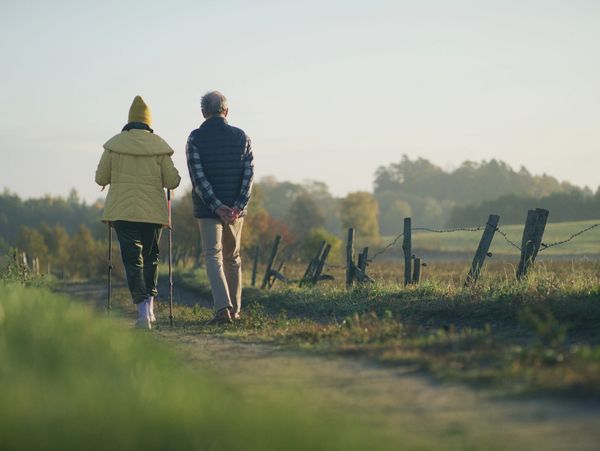 Two elderly people walking on a rural path with walking sticks.