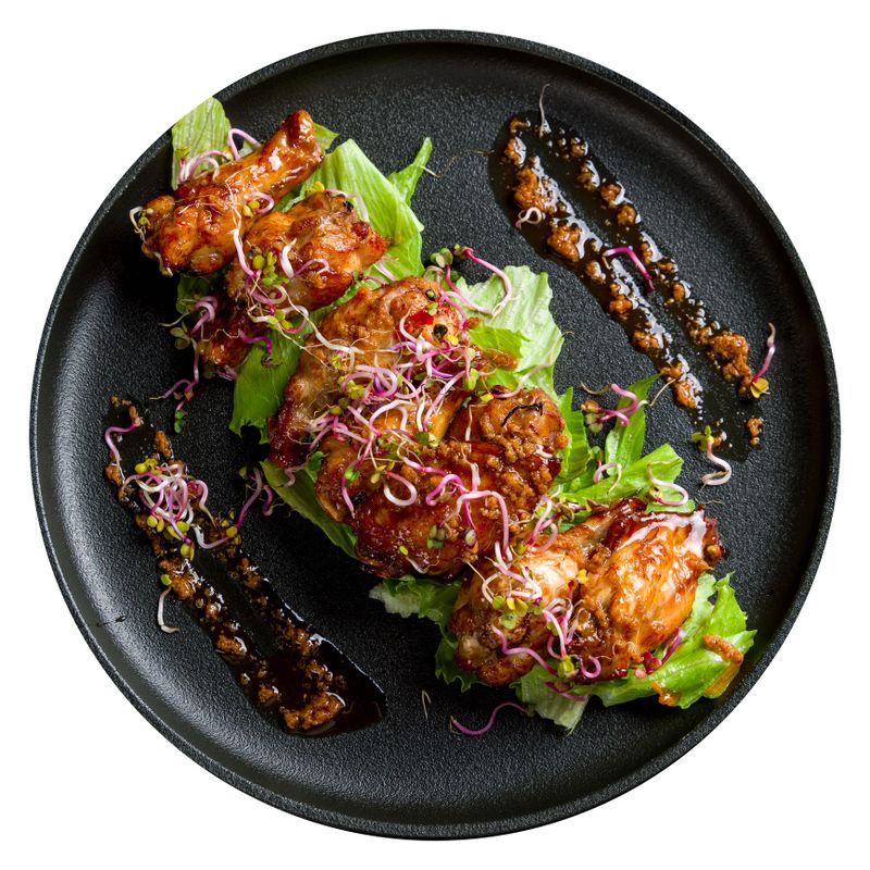 Chicken wings in sweet chili sauce on black plate top view isolated on white background