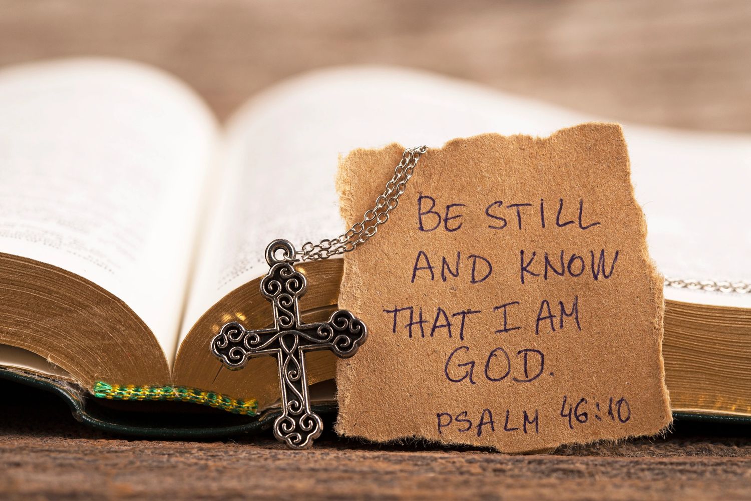 Open Bible with a cross necklace and a note quoting Psalm 46:10.