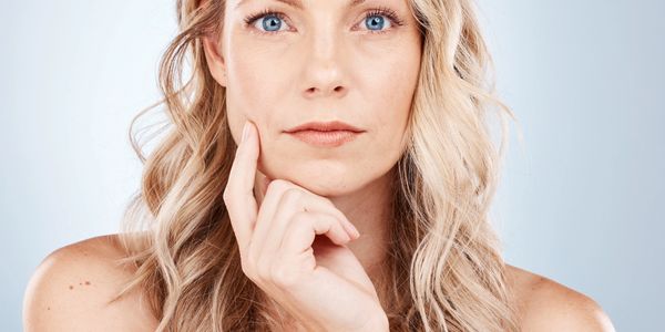 Blonde woman with blue eyes thoughtfully touching her face.