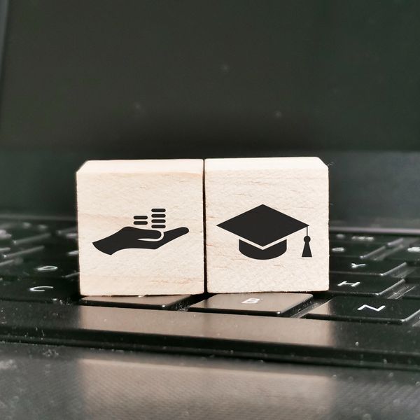 Wooden blocks with icons of money and graduation cap on a laptop keyboard.