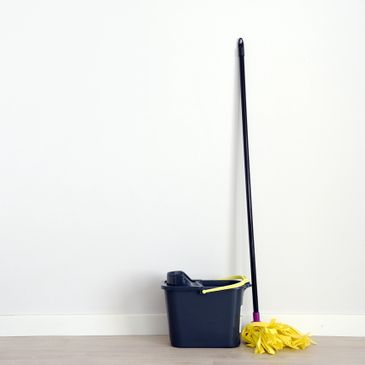 Yellow mop and black bucket against white wall.