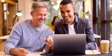 Two men smiling while working on a laptop together.
