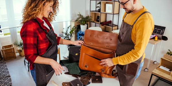 Two artisans examining a handmade leather bag in a craft workshop.