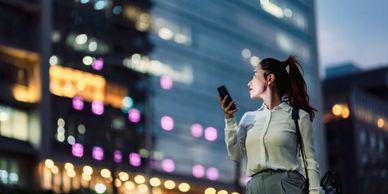 Woman looking at her phone in a city at night with blurred lights.