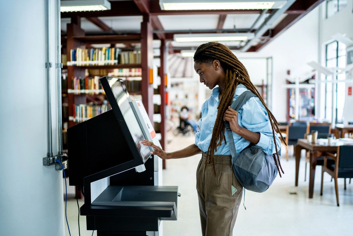 Young woman using a touchscreen kiosk in a library.