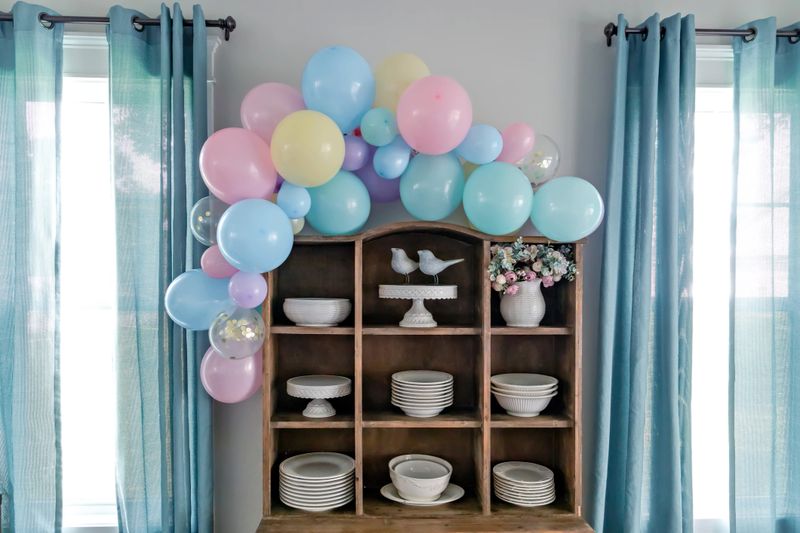 A vintage rustic wood china hutch decorated with a balloon arch in pastel colors for a baby shower or birthday party.