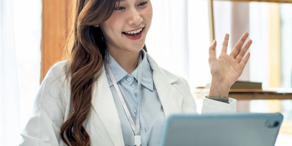Young female doctor video calling on a tablet, smiling and waving.