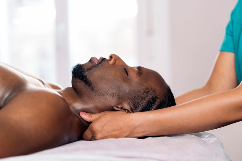 Relaxed black man lying down and receiving a neck massage. The masseuse is using oil massage.