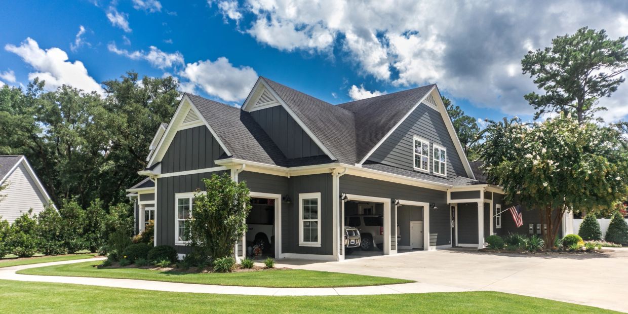 Grey house with manicured lawn and garage under blue sky.