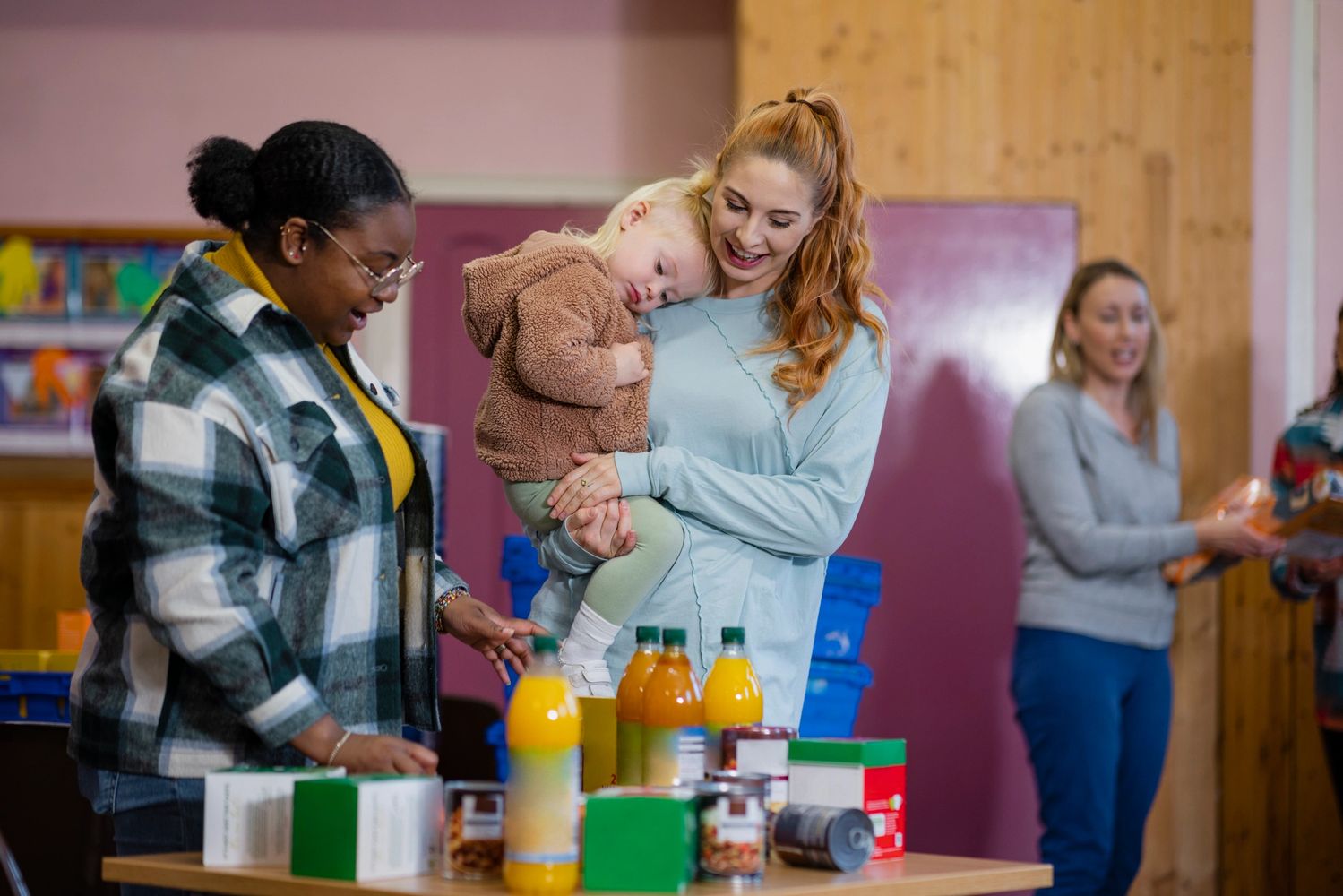Women and child at a community food donation center with various food items on a table.