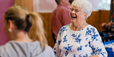 Elderly woman laughing joyfully in a social setting.