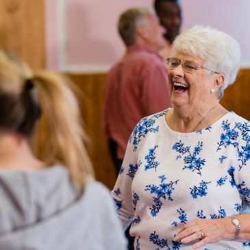 Elderly woman laughing joyfully in a social setting.