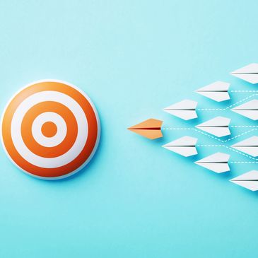 Orange paper airplane leading white ones toward an orange target on blue background.