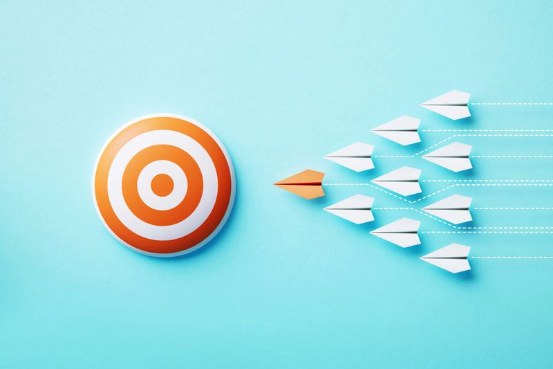 Paper planes flyıng towards an orange bull's eye target on blue background, Target concept.