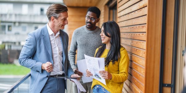 Three people discussing paperwork outdoors.