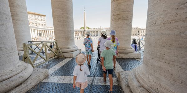 Children walking through large stone columns in a historic square.