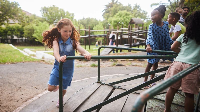 Little girl pushing a merry-go-round for friends while playing together outside in a park in summer
