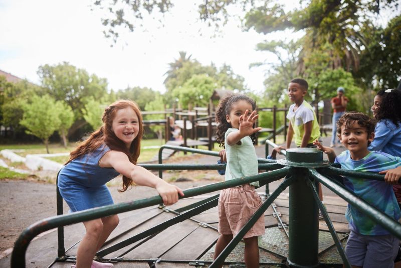 Laughing group of diverse little children playing together on a merry-go-round outside in a park in summer