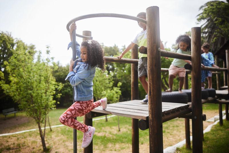 Diverse group of smiling little children playing together on a jungle gym in a park in summer