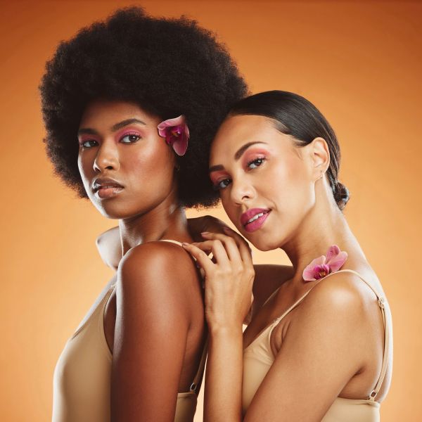 Two women with flowers posing against an orange background.