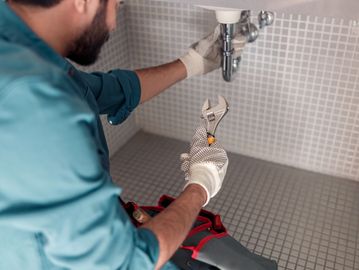 A plumber fixing a sink pipe with a wrench and gloves.