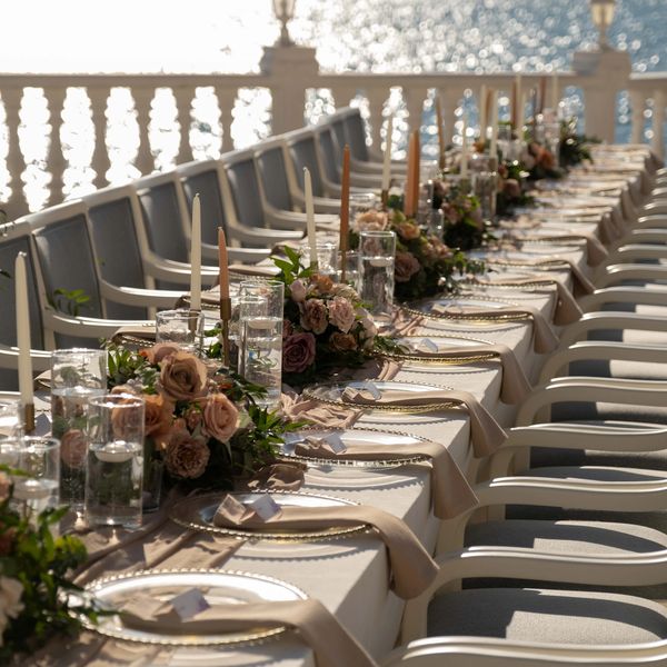 Elegant outdoor dining table set by the sea with flowers and candles.