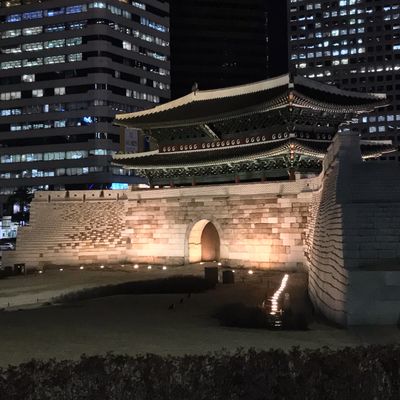 Night view of a traditional Korean gate with modern buildings in the background.