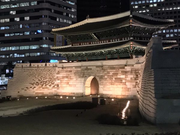 Illuminated traditional gate in a modern city at night.
