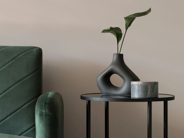 Modern minimalist side table with unique vase and green armchair.