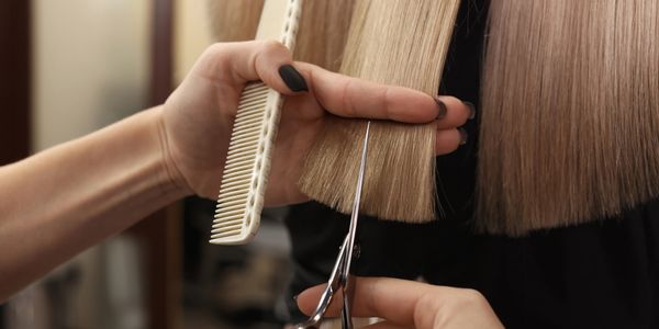 Close-up of a hairdresser trimming straight blonde hair with scissors and a comb.