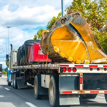 Flatbed truck carrying large construction equipment on highway.
