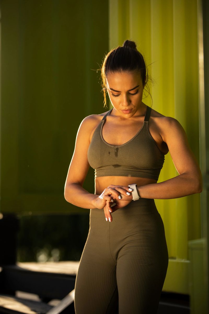 Young female runner making break outdoor and checking time and pulse on the smart watch after intense training workout